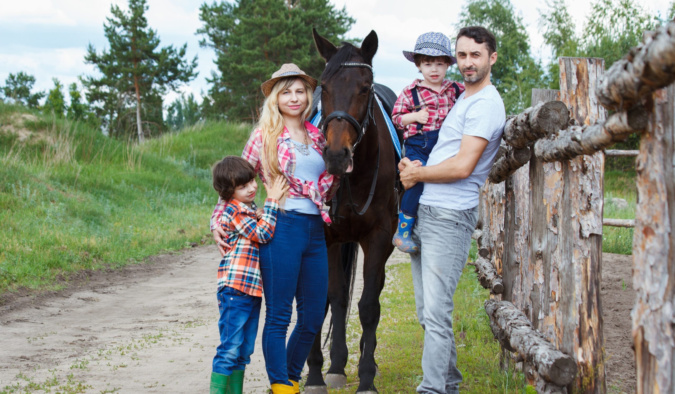 a family of four on a dirt road in a country setting. a mom with long wavy hair standing next to and hugging a horse that stands just a bit taller than her. The son is standing on the other side of his mom. The Dad stands on the other side of the horse with a smaller child in his arms. All are smiling and looking at the camera because they are happy knowing they are wearing minus bite all natural bug spray and the horse was just wiped down.