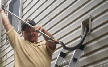 A man pulling a big snake out of the dryer vent located on the outside of the house.