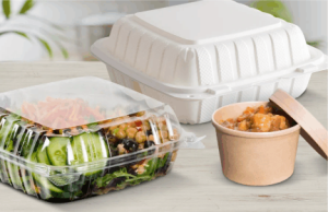 To go food on a table: A see through container with a fluffy green salad, a closed white container and an open soup container full of fresh soup. 